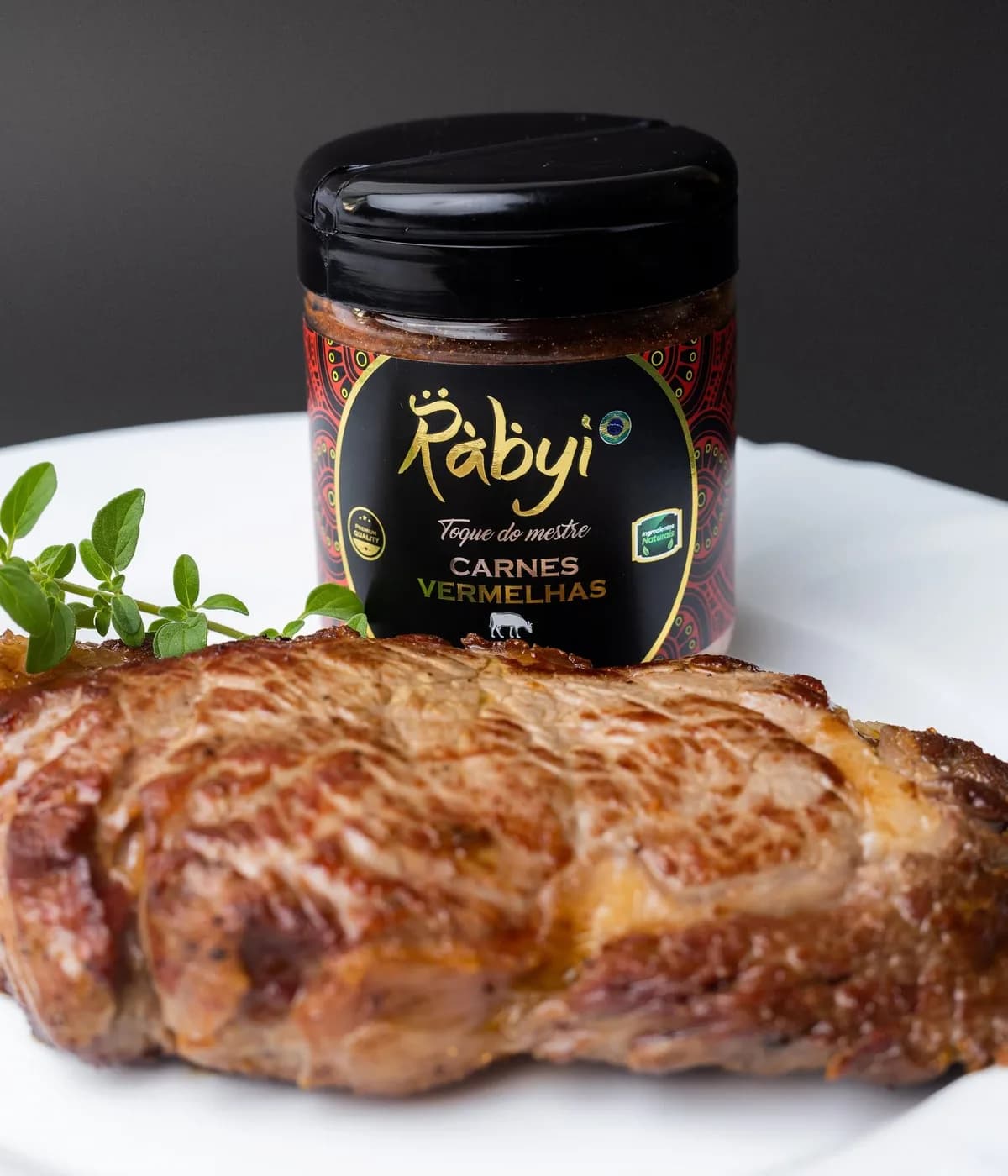 Tempero Carnes Vermelhas da linha Artesanal Rabyi ao lado de um preparo.