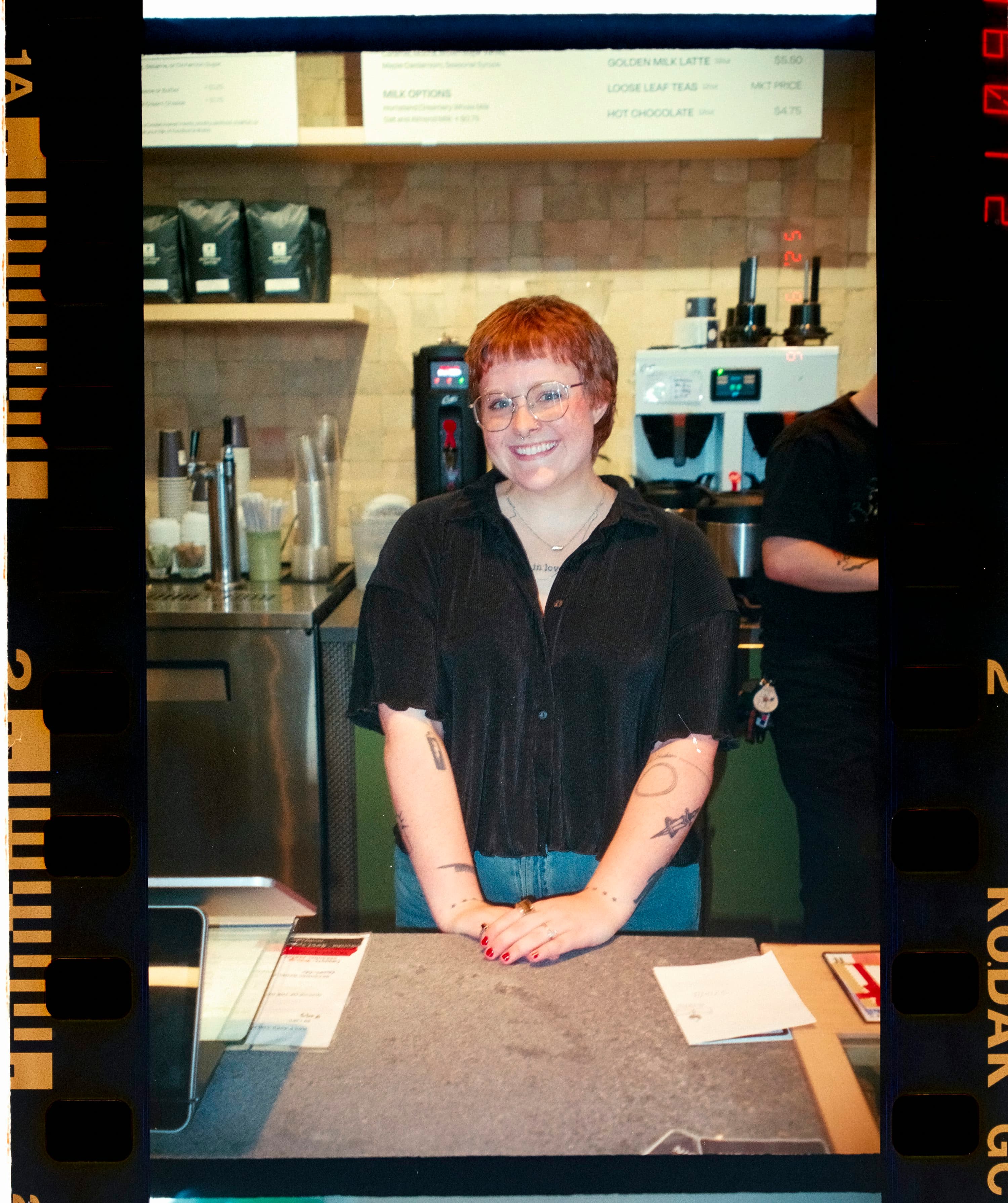 Profissional sorrindo atrás do balcão de um café; imagem ilustrativa